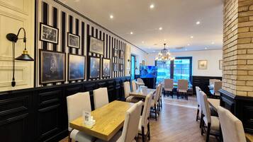 A restaurant with a black and white striped wall, framed pictures, and a wooden table with chairs.