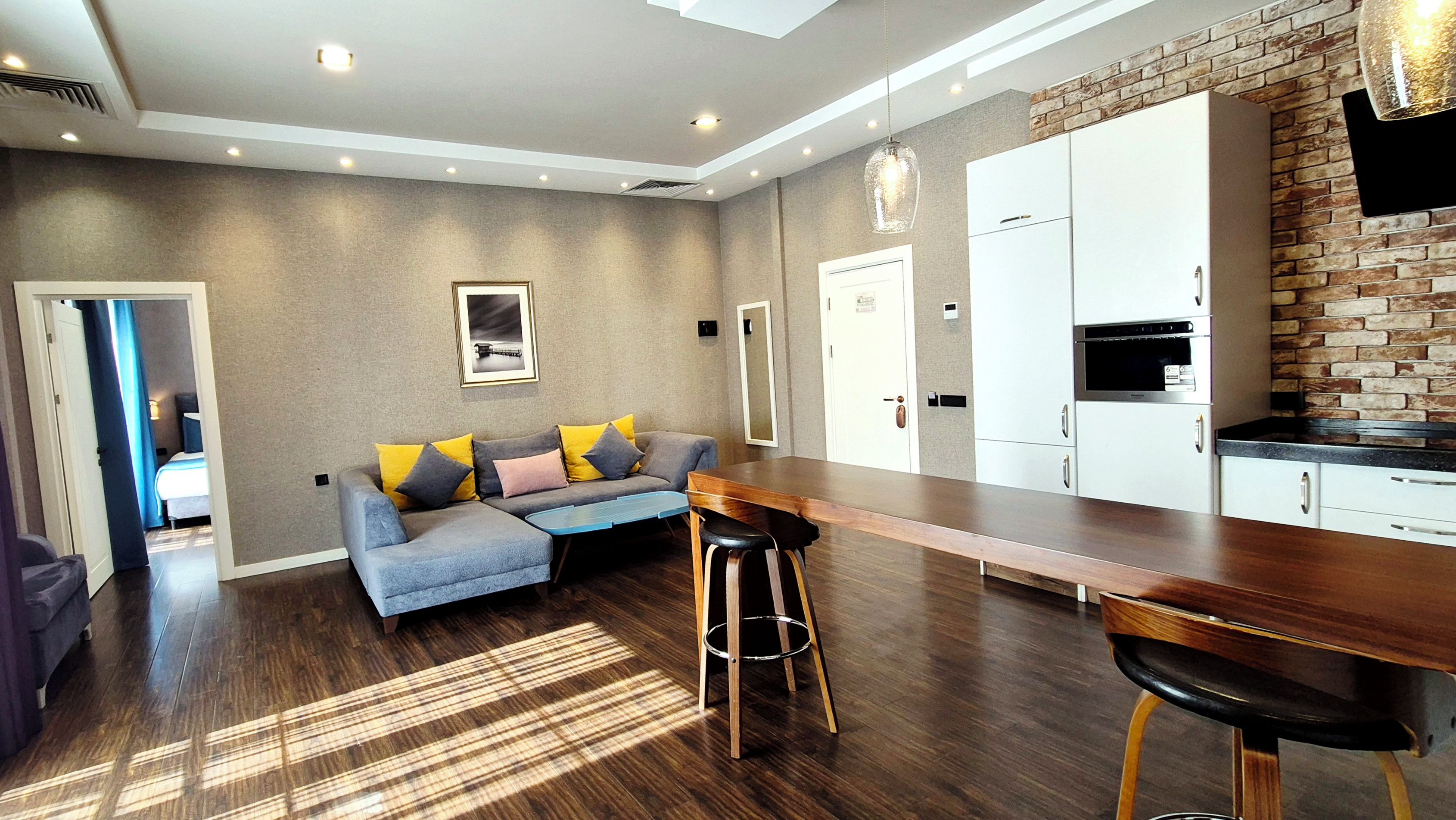Un espace de vie moderne comprenant un canapé, une table à manger et un coin cuisine avec des meubles blancs et un mur d’accent en briques.