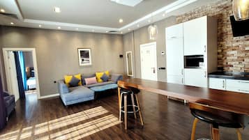 A modern living area with a sofa, a dining table, and a kitchen area with white cabinets and a brick accent wall.