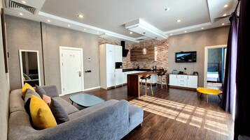 Uma sala de estar moderna com um sofá cinza, uma mesa de centro e uma TV fixada na parede.