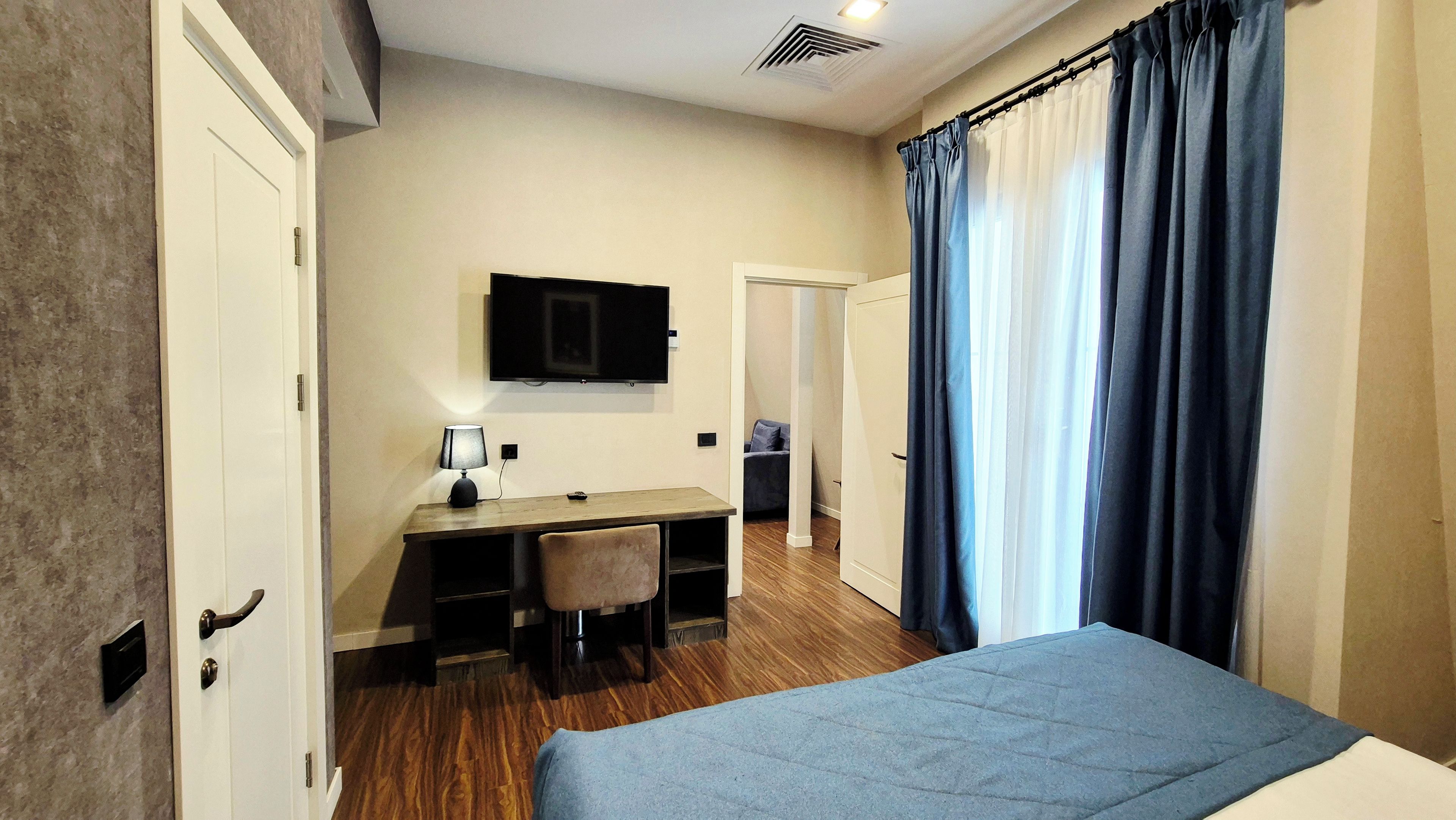 Une chambre à coucher avec un lit, un bureau avec une chaise, une télévision et une fenêtre avec des rideaux.