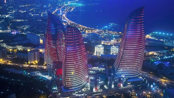 A cityscape at night with three prominent, illuminated skyscrapers with a curved design. - Port Rivoli Baku Hotel (Baku)