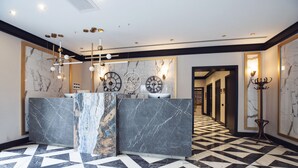 A hotel lobby with a marble reception desk, geometric patterned floor, and wall-mounted clocks.