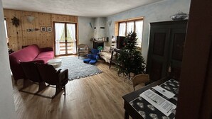 A cozy living room with a wooden floor, a sofa, a coffee table, a small Christmas tree, and a dining table with papers.
