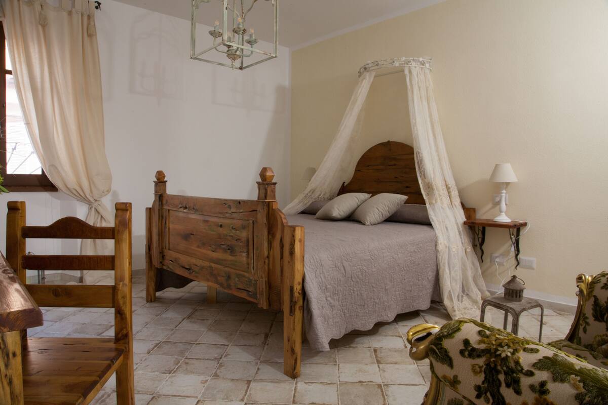 Une chambre à coucher avec un lit en bois, une chaise en bois, une petite table et une table de chevet.