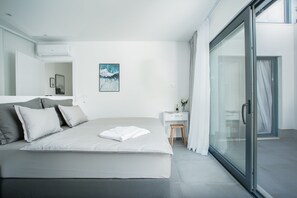 Moderni hotellihuone, jossa on suuri sänky, pieni työpöytä ja liukuovet, jotka johtavat lasiterassille.