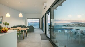 A modern dining area with a view of the sea, a glass-enclosed balcony, and a dining table set for two. - The Olive Exclusive holiday home (Okrug)