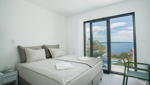 A bedroom with a large bed, a nightstand, a chair, and a view of the sea through a sliding glass door. - The Olive Exclusive holiday home (Okrug)