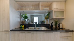 A modern kitchen with light wood cabinets, a black countertop, and stainless steel appliances.