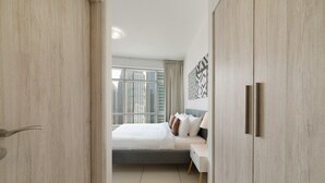A modern hotel room with a large bed, a bedside table, and a view of tall buildings through the window.