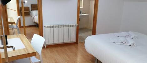Un dormitorio con cama, escritorio, silla, radiador y televisor en la pared.