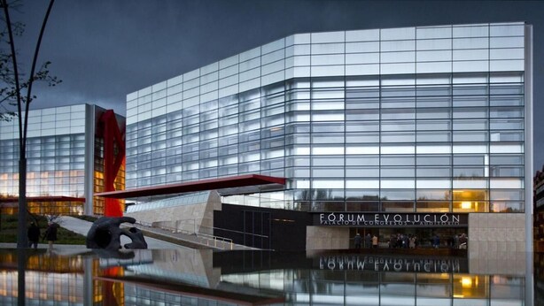 A modern building with reflective glass windows and a prominent red sculpture in front.