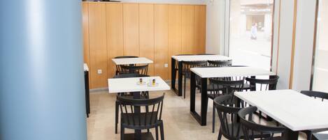 A dining area with multiple tables and chairs, a television mounted on the wall, and a view of the street outside.