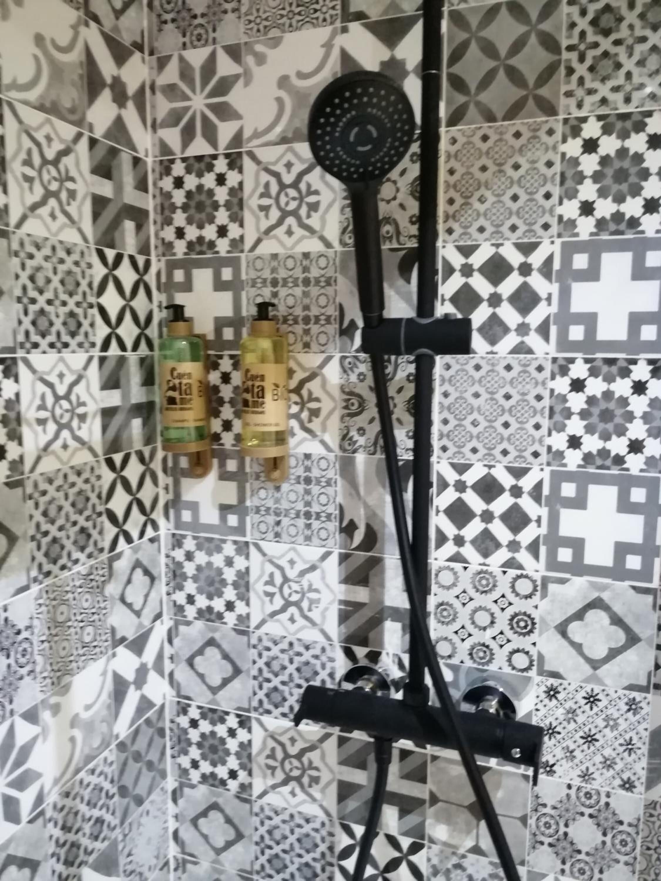 A shower with a black hose and a handheld showerhead, mounted on a wall with patterned tiles.