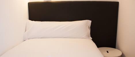 Una cama bien hecha con ropa de cama blanca y cabecera negra.