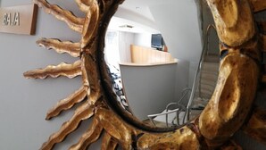 A sun-shaped mirror with a wooden frame reflecting a room with a desk and a chair.