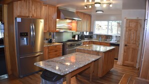 A kitchen with wooden cabinets, stainless steel appliances, granite countertops, and a wooden floor.