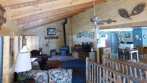 A wooden cabin interior with a high ceiling, a fireplace, a television, and a dining area.
