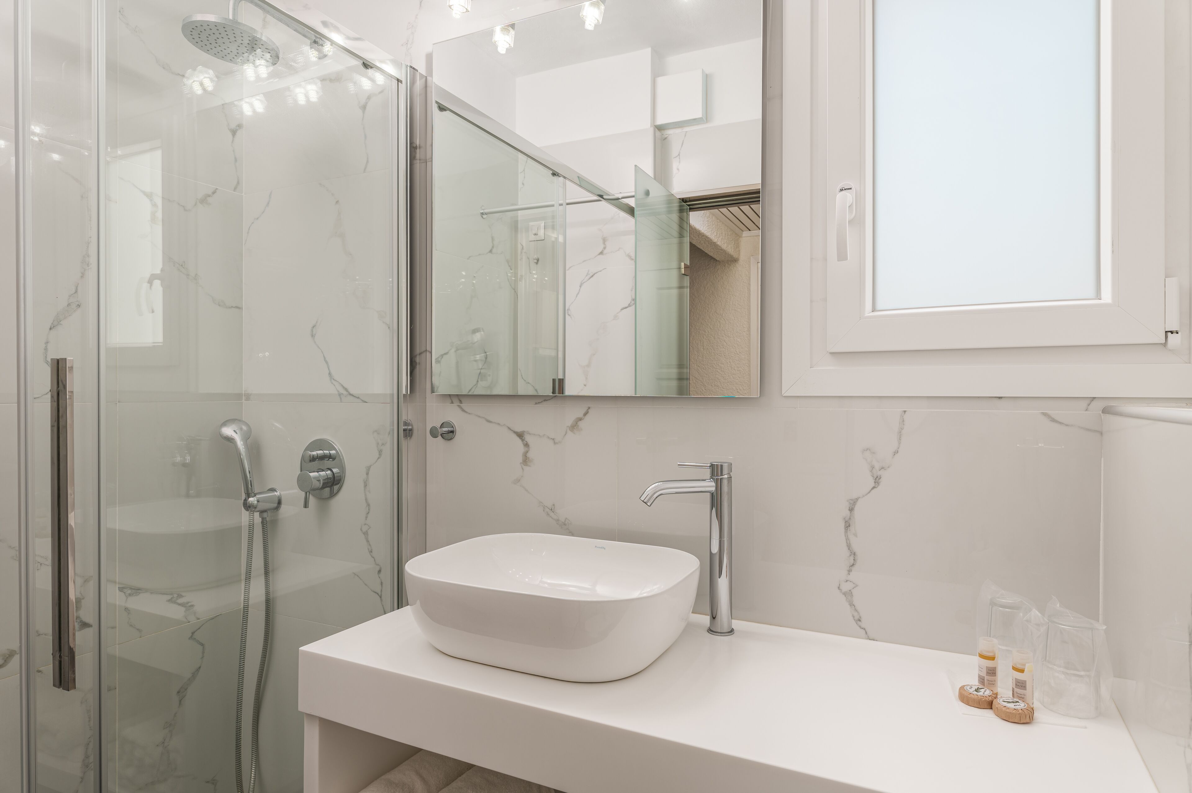 A modern bathroom with a glass-enclosed shower, a white sink, and a large mirror.