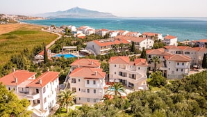 A coastal residential area with multi-story buildings, a swimming pool, and a view of the sea and a mountain in the distance.