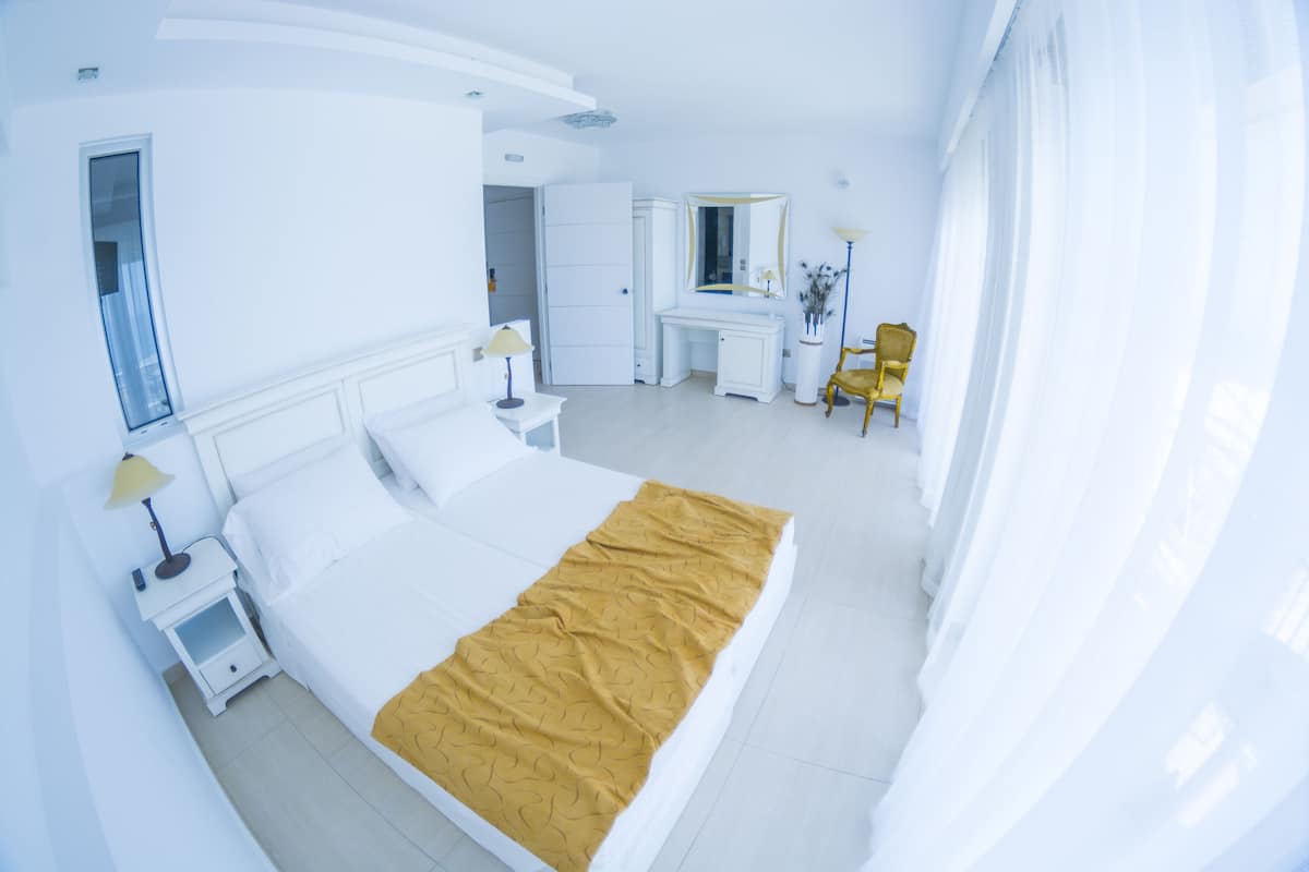 A hotel room with a large bed, a desk, a chair, and a wardrobe.