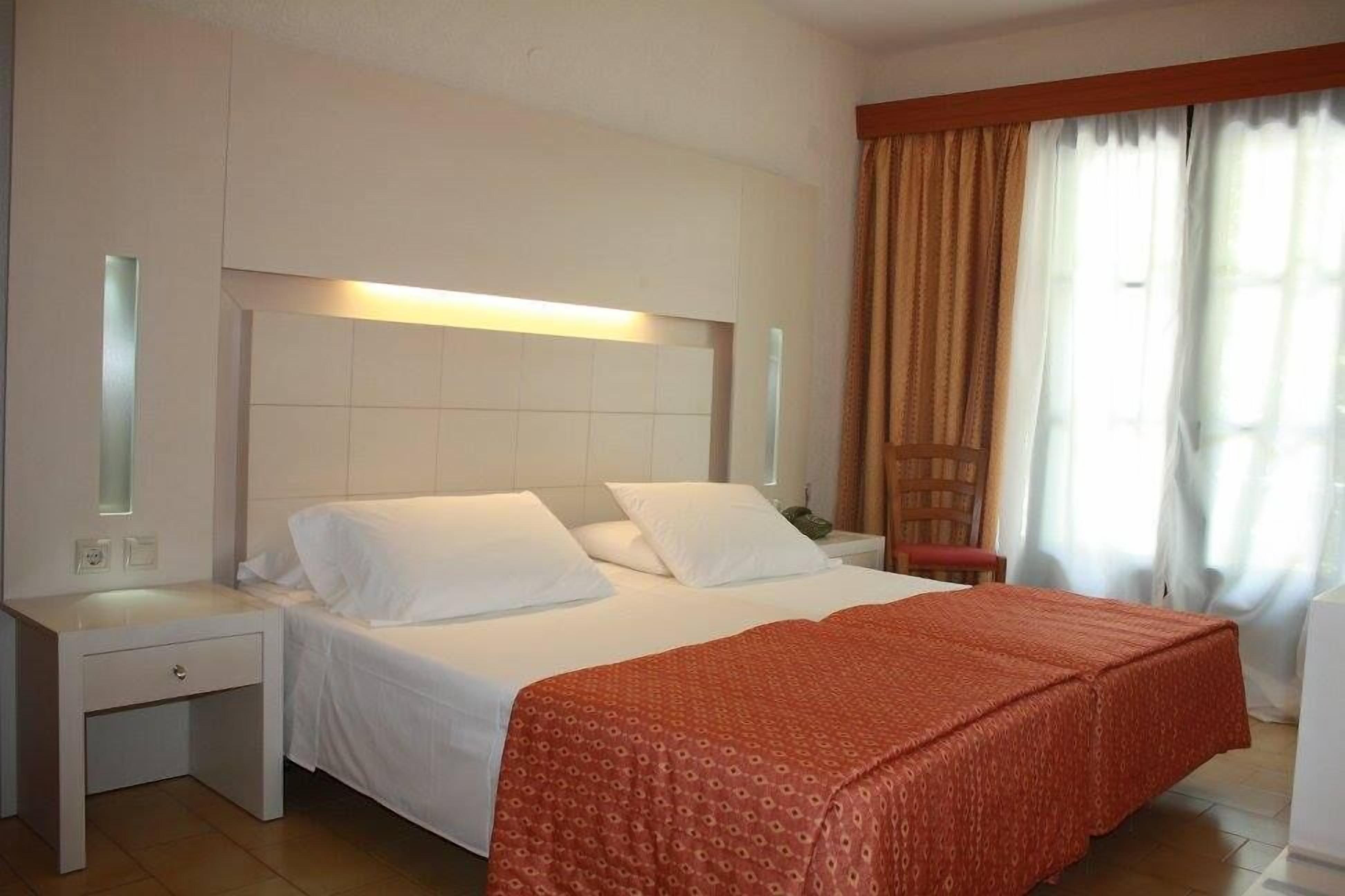 A hotel room with a bed, nightstands, a desk, and a window with curtains.