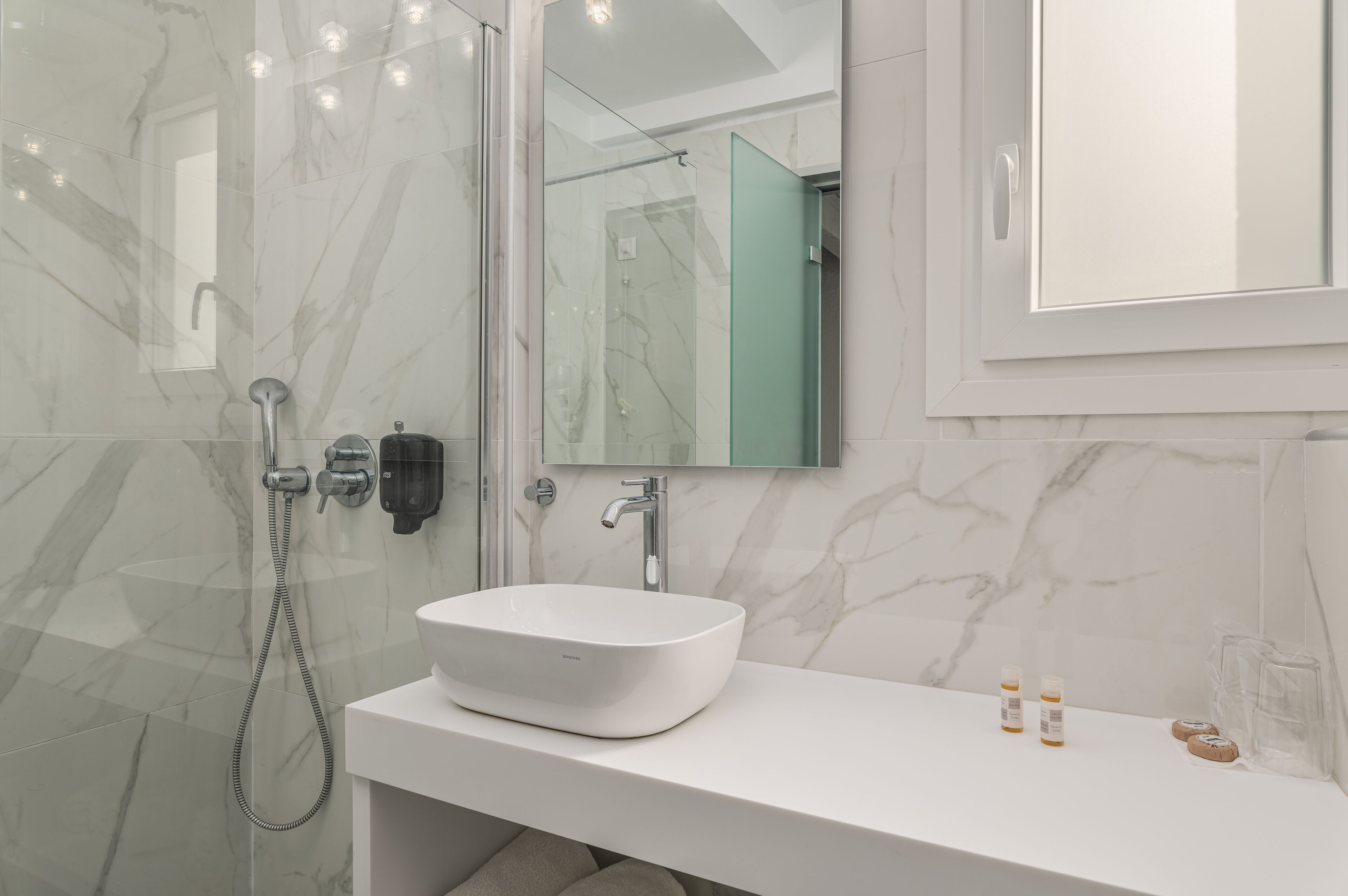 Un baño moderno con un lavabo blanco, cabina de ducha de vidrio y un espejo grande.
