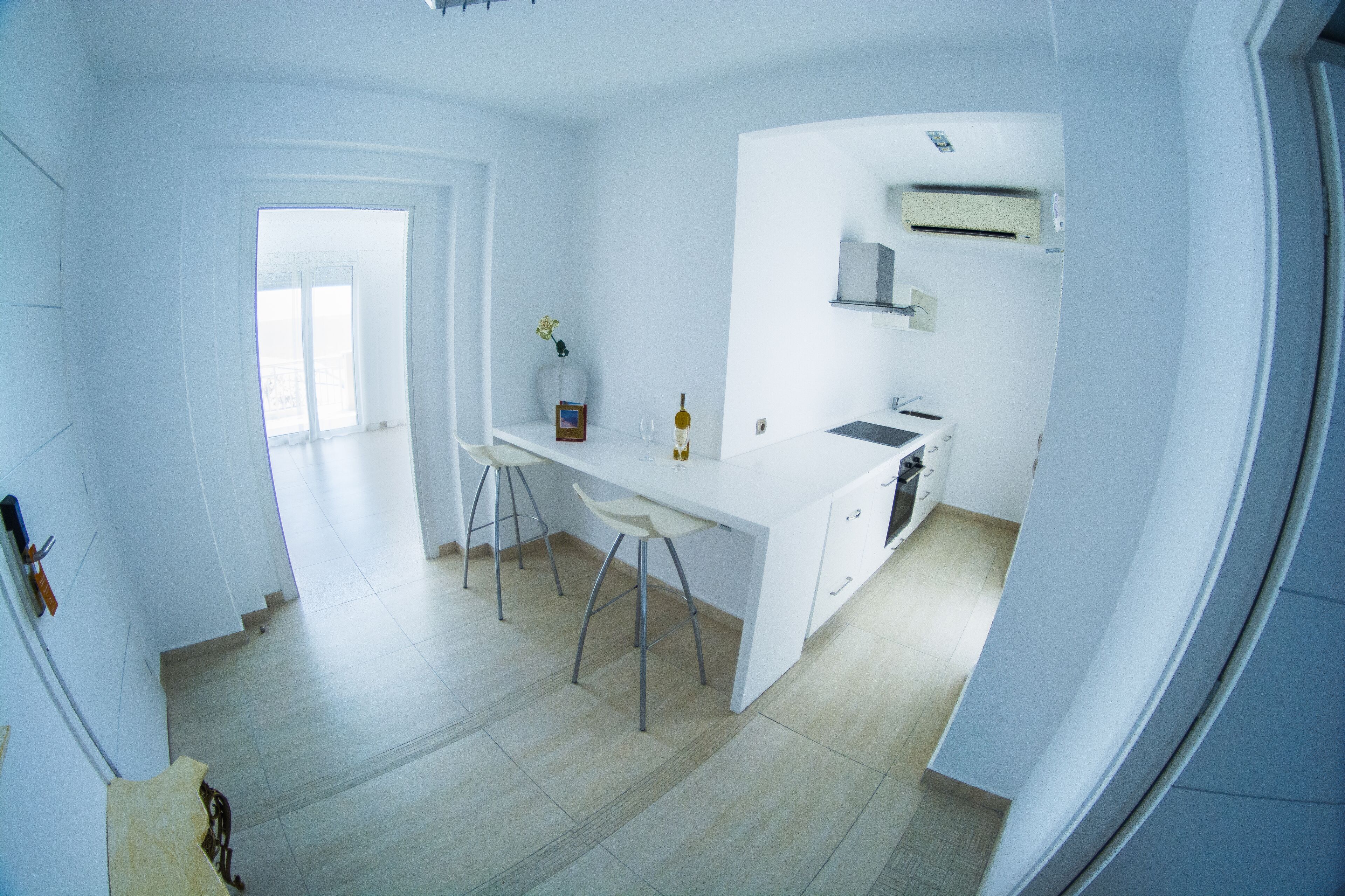 A modern kitchen with white cabinetry, a central island with stools, and a built-in oven.