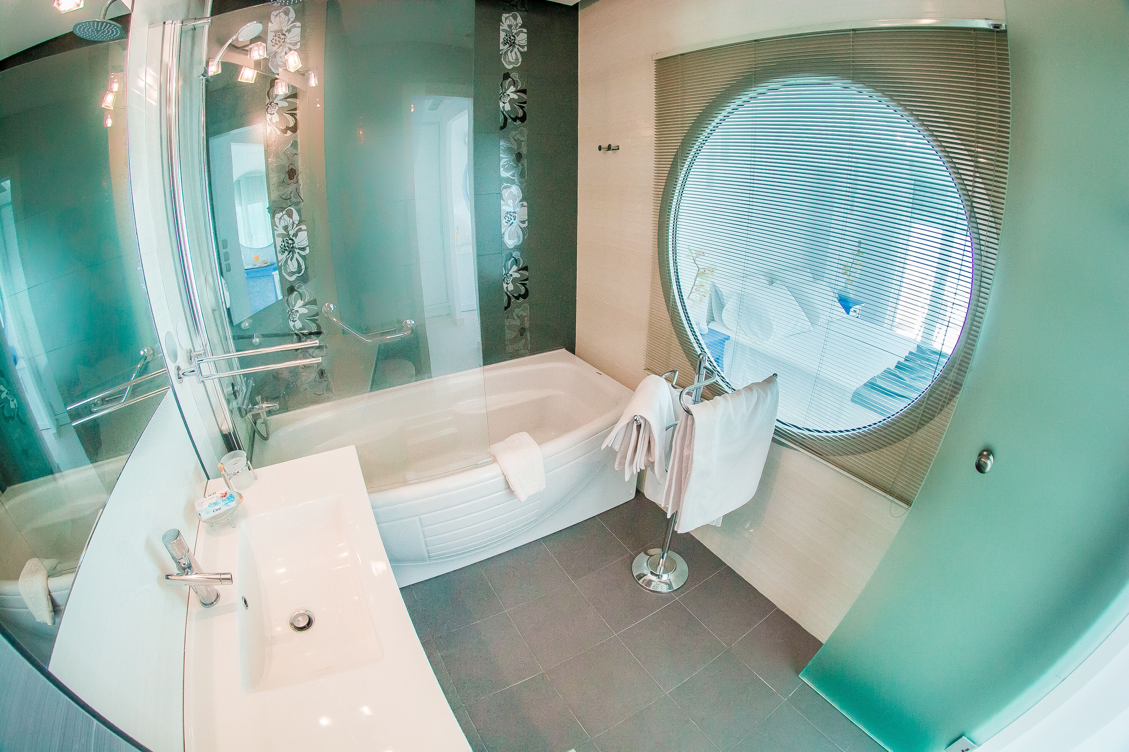 A modern bathroom with a large bathtub, a glass-enclosed shower, and a round window.
