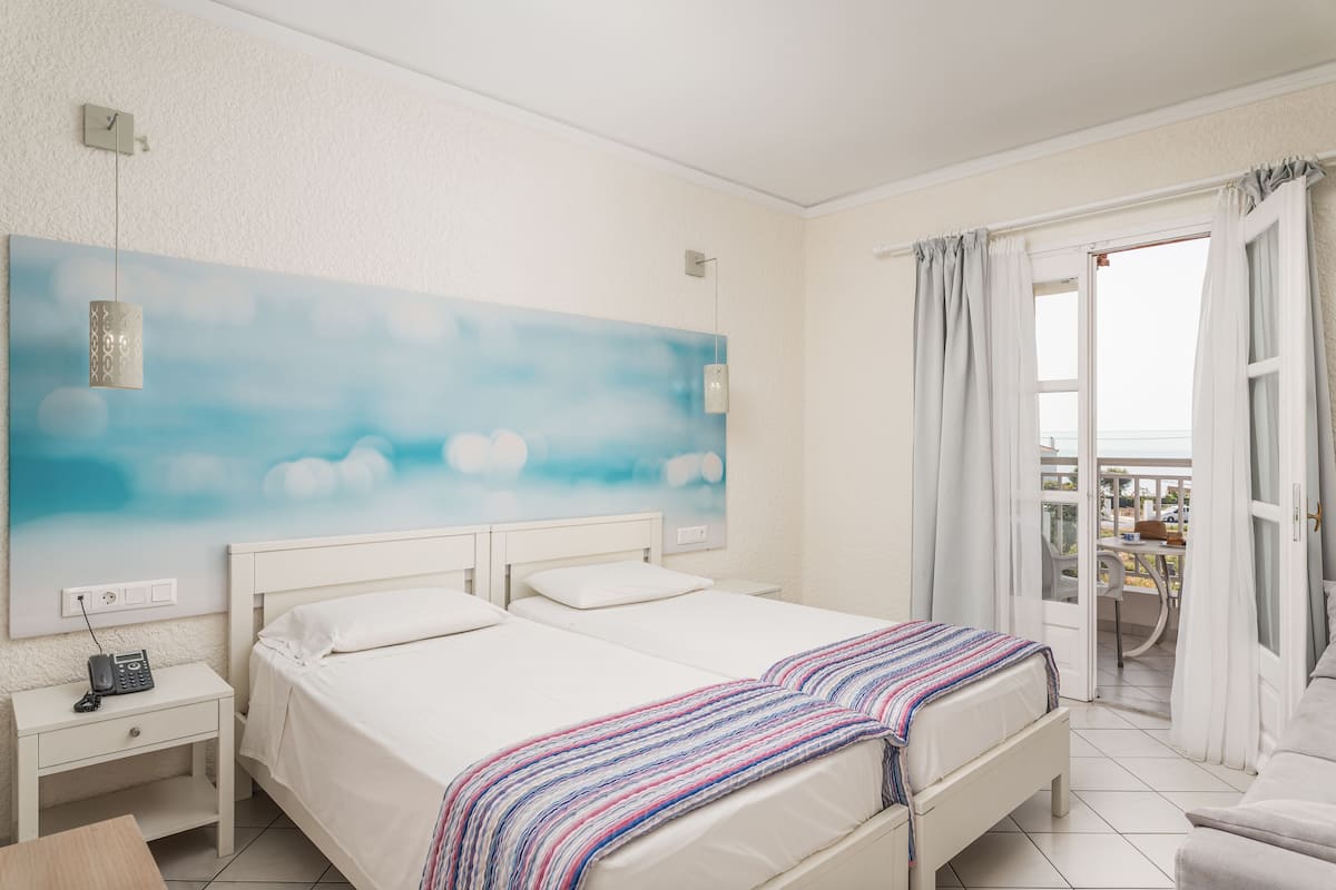 A hotel room with a bed, bedside tables, a painting, and a balcony with curtains.