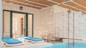 An indoor swimming pool with lounge chairs, a table, and a ceiling with wooden beams.