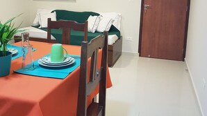 A dining area with a table set for two, a window with blinds, a door, and a small potted plant. - Apartment between the airport and the beach. (Boa Viagem)