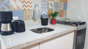 A kitchen with a granite countertop, a coffee maker, a toaster, a sink, a red potted plant, and a gas stove. - Apartment between the airport and the beach. (Boa Viagem)