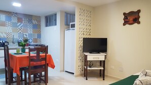 A compact living space with a dining area, a kitchenette, a TV on a stand, and a bed. - Apartment between the airport and the beach. (Boa Viagem)