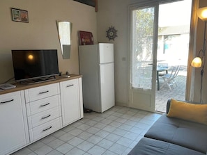 Espaço compacto com cozinha compacta, televisão, frigorífico e porta de correr que dá para uma área externa.