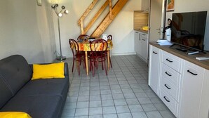 Espai vital compacte amb sofà, taula de dinar, cadirees, televisió i zona de cuina.