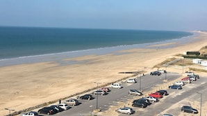 En parkeringsplads ved siden af en strand, med biler parkeret og frit udsyn til havet.