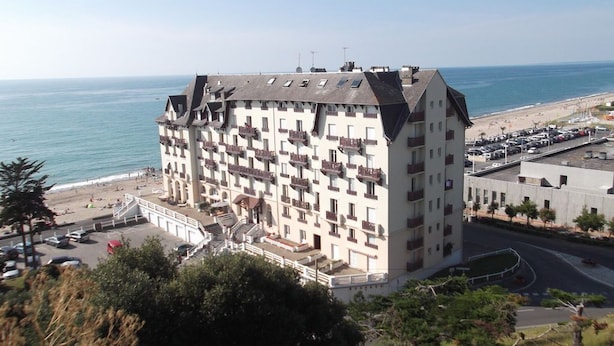 Et hotel med flere etager, altaner, udsigt til stranden og en parkeringsplads.