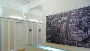 Un hall d’hôtel avec un comptoir d’accueil, une grande photographie représentant un paysage urbain accrochée au mur et une rangée de portes blanches.