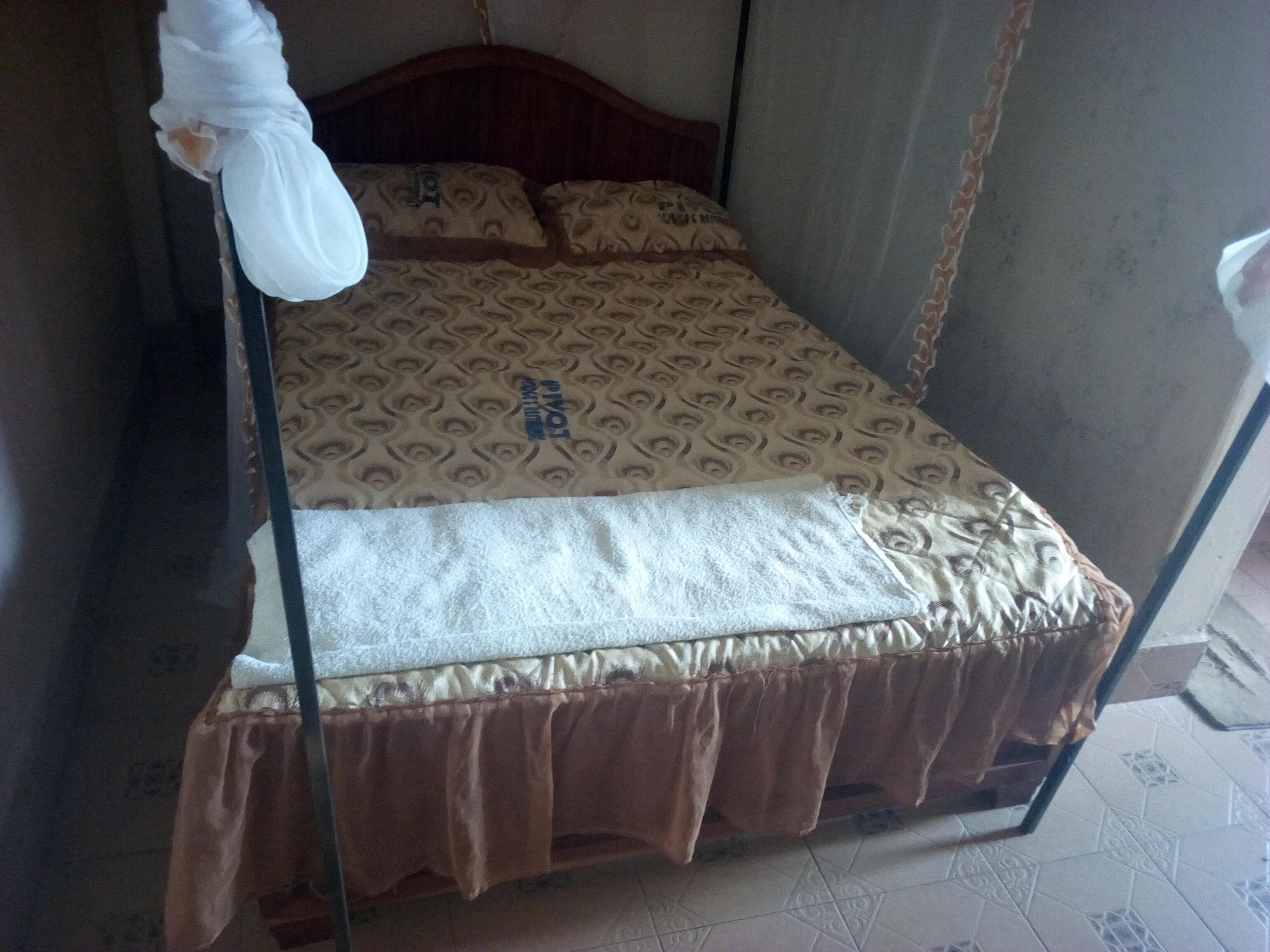 A bed with a patterned bedspread, a brown skirted bed skirt, and a white hanging object.