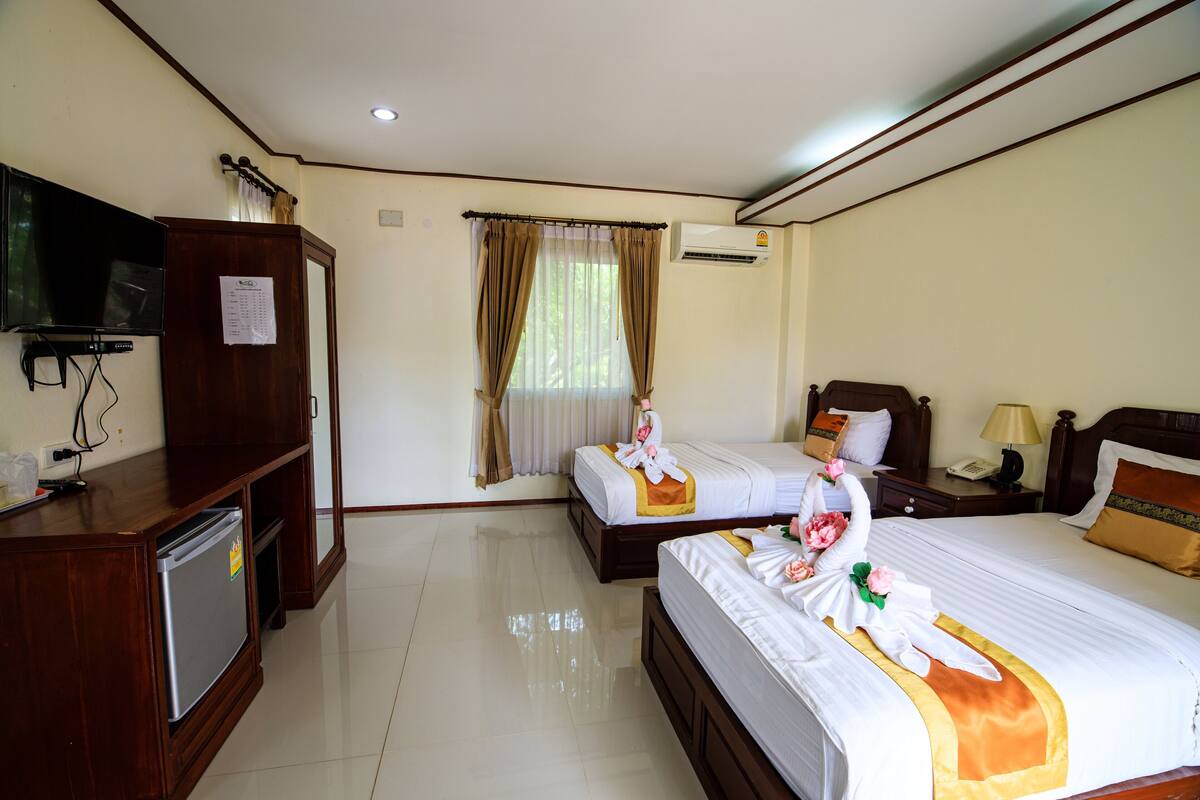 Habitación de hotel con dos camas, televisión, escritorio y refrigerador, y aire acondicionado.