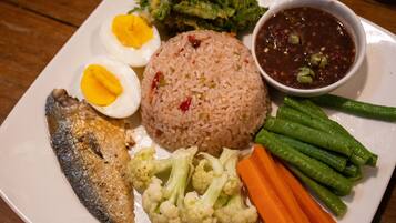 Um prato com arroz, ovo cozido, peixe, legumes e um acompanhamento de molho.