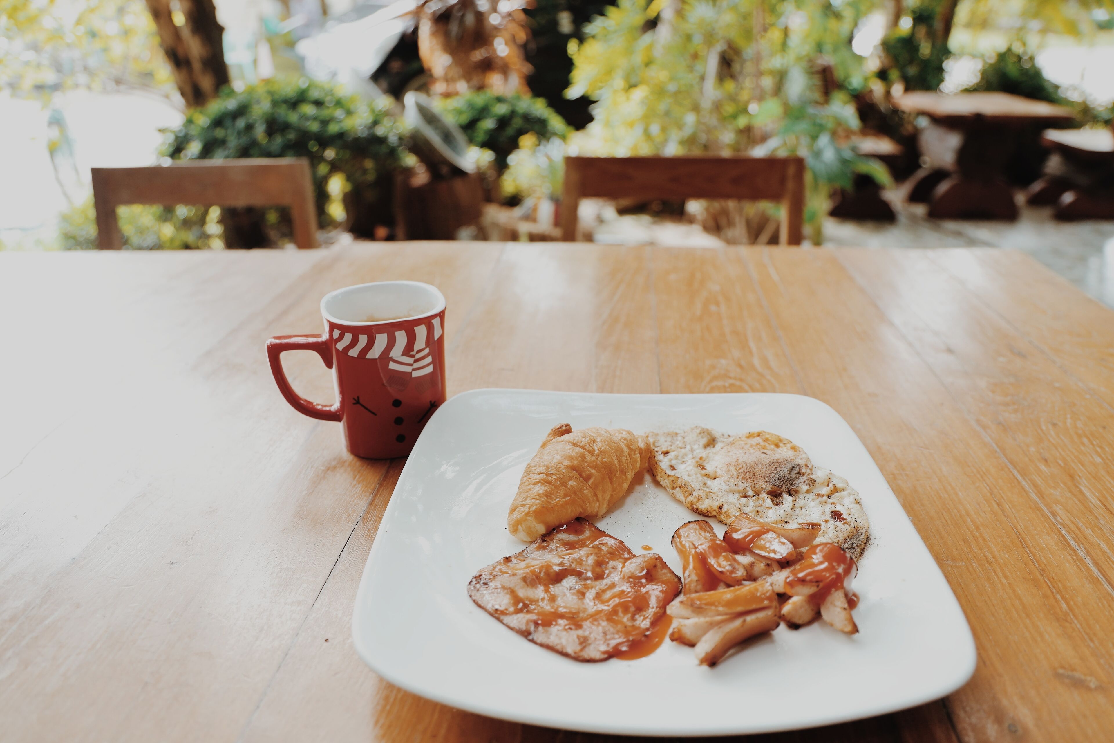 Una mesa de madera con un plato de comida y una taza roja.