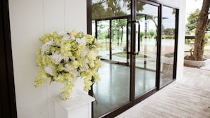 A white wall with a large window and a white pedestal with a floral arrangement. - Onesook Resort Sukhothai (Sukhothai)