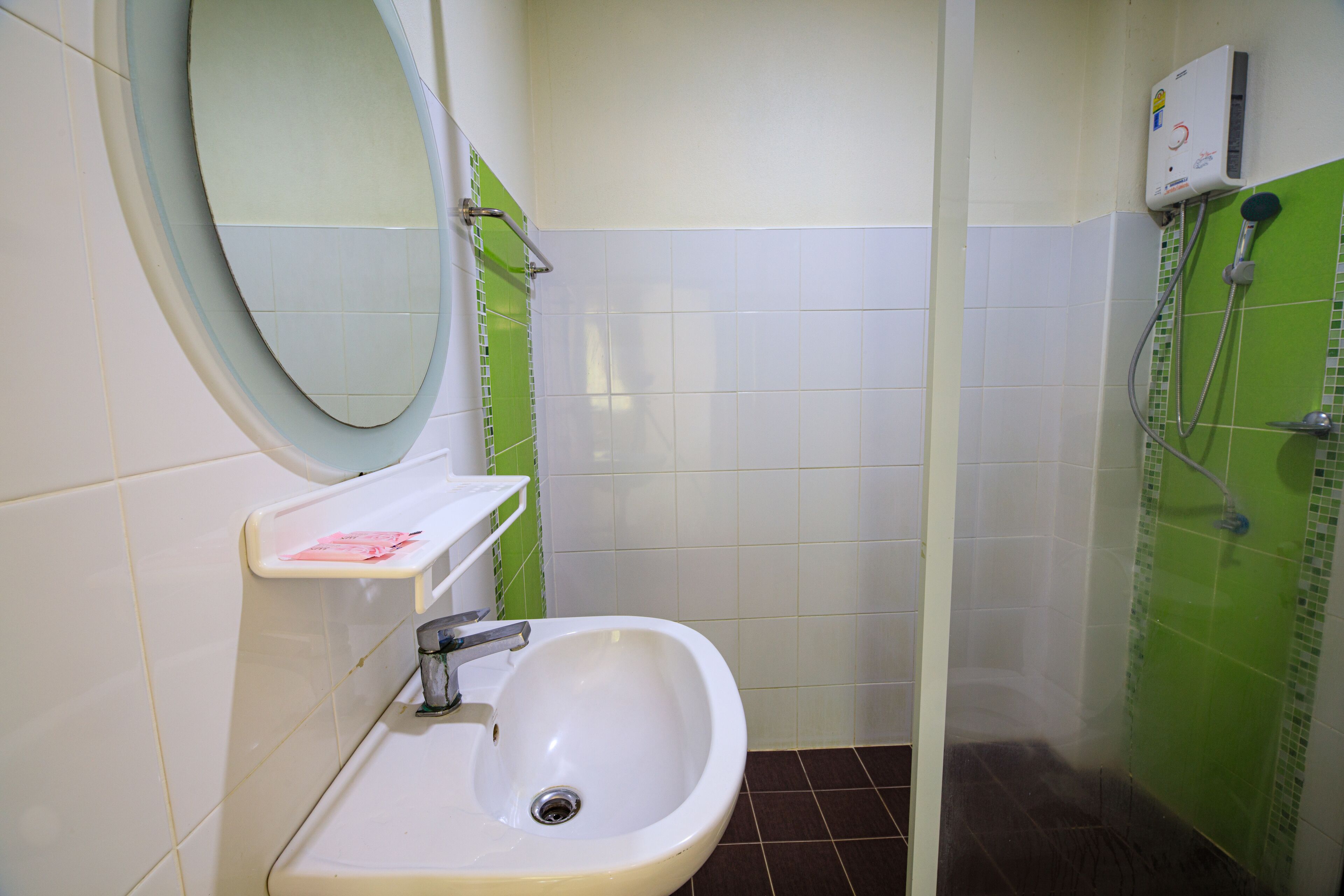 Un baño con un lavamanos blanco, un espejo y una zona de ducha con azulejos verdes.