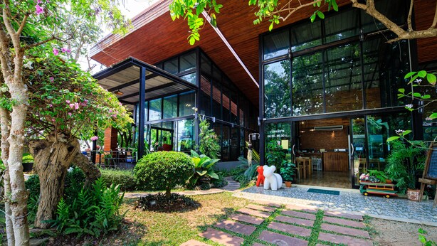 A modern building with large glass windows, a stone pathway, and lush greenery. - Onesook Resort Sukhothai (Sukhothai)