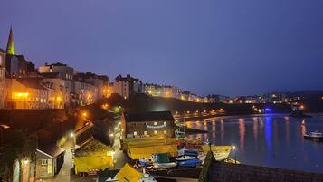 A coastal town at dusk with buildings, a church spire, and boats docked along the waterfront.