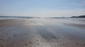 A wide beach with wet sand and footprints, a clear sky, and distant hills.