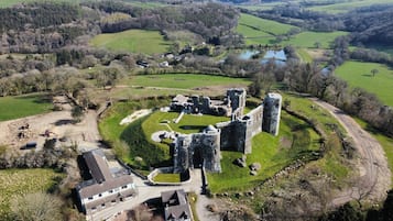 A historic castle with ruins, surrounded by green fields and a small village.