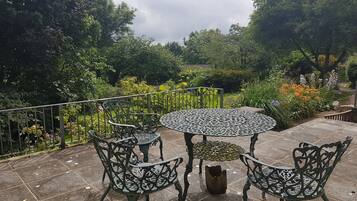 An outdoor patio with a round table and four chairs, surrounded by lush greenery and flowering plants.